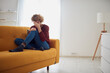 © astrosystem - Woman with knee and headache problem sitting on a couch at home.