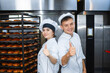 © salomonus_ - Young guy and girl bakers on the background of an industrial oven in a bakery show thumb up.