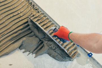 Close up of the hands of a master builder's man with a notched trowel, putting a tile adhesive mixture, performs the installation of ceramic tiles
