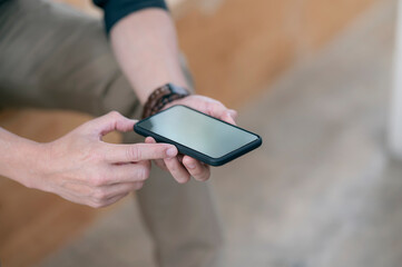 Wall Mural - closeup shot of man hands holding blank screen smartphone while sitting outdoors, shallow depth of f