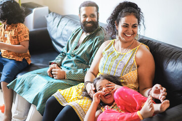 Wall Mural - happy indian family having fun at home sitting on sofa - focus on mother