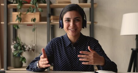 Canvas Print - Smiling pleasant young beautiful mixed race indian woman in headphones gesturing, holding video call conversation with colleagues, discussing project or coaching mentoring students distantly.