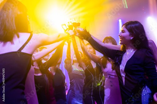 Young people celebrating a party, drink and dance . Group of friend toasting drinks while having fun at the disco club at night . Friendship and nightlife concept .