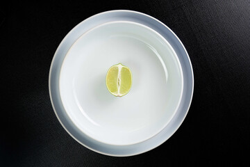 Lime slice on white plate on black background