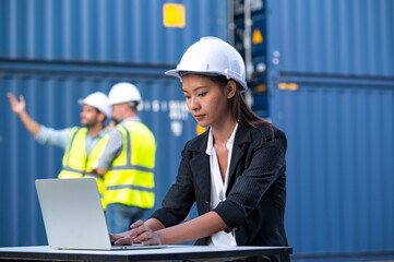 Wall Mural - Woman logistics worker  wear safety helmets and protect suite working and checking product with laplets in shipping container, commercial transport background.