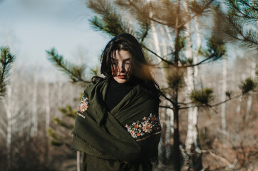 Wall Mural - Woman wrapped in an embroidered forest green scarf walking in the forest