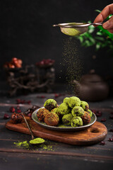 Matcha energy sweets balls made of dried fruits dusted with bright green matcha powder on rustic wooden table, dark background. Raw vegan healthy candies - dessert. Copy space.