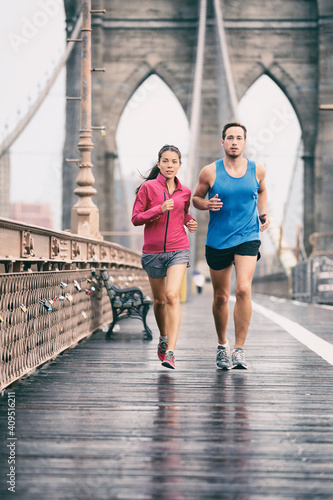 New York city runners athletes training jogging on Brooklyn Bridge for Marathon race, fit couple on outdoor summer run jog. Vertical background.