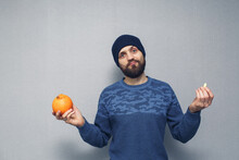 A Bearded Guy Holds An Orange And A Suppository For Hemorrhoids In His Hands. Hemorrhoids Concept.