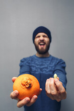 A Man Screams In Problems Due To Hemorrhoids. A Bearded Guy Holds An Orange And A Suppository For Hemorrhoids In His Hands. Hemorrhoids Concept.