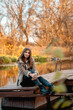 © Дмитрий Ткачев - Beautiful woman sitting by the lake and enjoying the beauty of golden autumn