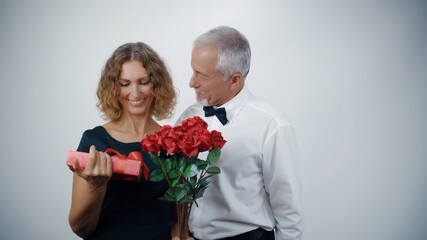 Wall Mural - A loving elderly husband presents a gift and roses to a mature smiling woman.