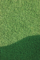 Artificial grass fake turf synthetic lawn field macro closeup gentle shaded shadow area, green sports astroturf texture, vertical textured background pattern, large detailed horizontal shade