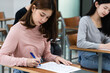 © EduLife Photos - Young female university students concentrate on doing examinations in the classroom. Girl students seriously write the exercise of the examinations in the classroom.