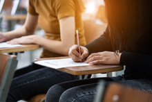 Young Female University Students Concentrate On Doing Examinations In The Classroom. Girl Students Seriously Write The Exercise Of The Examinations In The Classroom.
