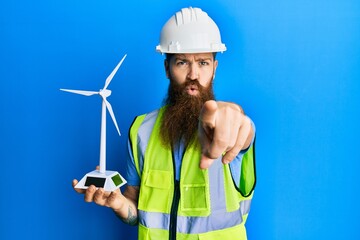 Sticker - Redhead man with long beard holding solar windmill for renewable electricity pointing with finger to the camera and to you, confident gesture looking serious