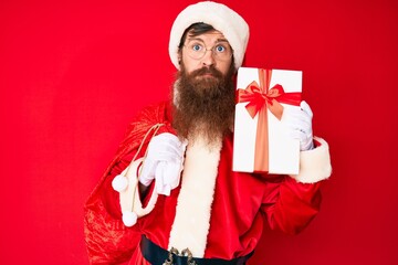 Canvas Print - Handsome young red head man with long beard wearing santa claus costume and big bag with presents skeptic and nervous, frowning upset because of problem. negative person.