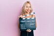 © Krakenimages.com - Beautiful caucasian blonde girl holding video film clapboard winking looking at the camera with sexy expression, cheerful and happy face.