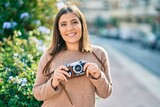 Fototapeta Paryż - Young hispanic tourist woman smiling happy using vintage camera at the city.