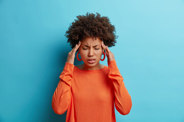 photo of frustrated young afro american woman has headache keeps hands on temples suffers unbearable