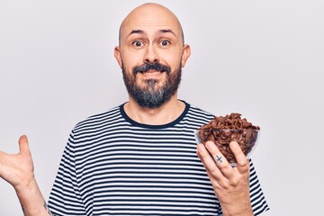 Wall Mural - Young handsome man holding chocolate cereals celebrating achievement with happy smile and winner expression with raised hand