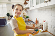 Little housewife. Portrait of a cute little girl in a bright apron washing dishes in a bright kitchen. Child loves to help his mother tidy up the house. Concept of kids learning to do domestic chores.