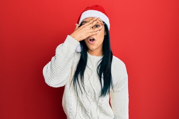 Sticker - Beautiful hispanic woman wearing christmas hat peeking in shock covering face and eyes with hand, looking through fingers afraid