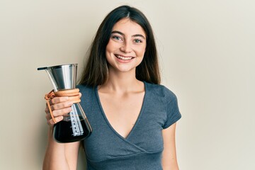 Poster - young caucasian woman holding coffee maker with filter looking positive and happy standing and smili