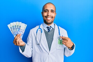 Canvas Print - Hispanic adult doctor man wearing medical uniform holding 100 south african rand smiling happy pointing with hand and finger