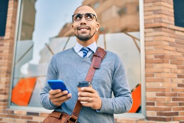 Wall Mural - Young african american businessman using smartphone and drinking take away coffee at the city.