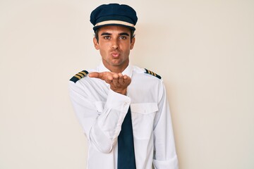 Sticker - Young hispanic man wearing airplane pilot uniform looking at the camera blowing a kiss with hand on air being lovely and sexy. love expression.