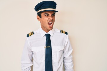 Sticker - Young hispanic man wearing airplane pilot uniform angry and mad screaming frustrated and furious, shouting with anger. rage and aggressive concept.