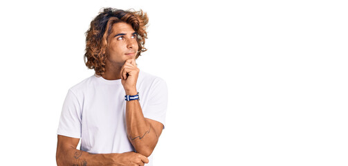 Young hispanic man wearing casual white tshirt with hand on chin thinking about question, pensive expression. smiling with thoughtful face. doubt concept.