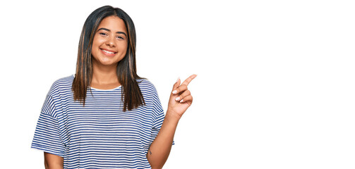 Young latin girl wearing casual clothes with a big smile on face, pointing with hand and finger to the side looking at the camera.