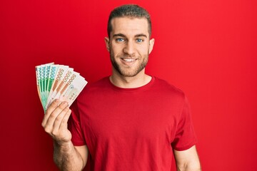 Sticker - Young caucasian man holding 5000 south korean won banknotes looking positive and happy standing and smiling with a confident smile showing teeth