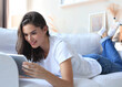 © ty - Beautiful young woman using tablet sitting on sofa at home at living room.