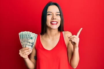 Poster - Young hispanic girl holding 20 dollars banknote smiling happy pointing with hand and finger to the side