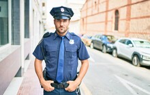 Young Handsome Hispanic Policeman Wearing Police Uniform. Standing With Serious Expression At Town Street.