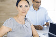 © Iryna - Businesswoman and businessman discussing questions while using a computer in modern office. Portrait of female latin american entrepreneur at meeting. Group of diverse people