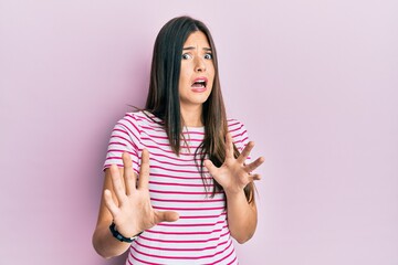 Wall Mural - Young brunette woman wearing casual clothes over pink background afraid and terrified with fear expression stop gesture with hands, shouting in shock. panic concept.