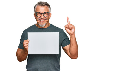 Sticker - Middle age grey-haired man holding blank empty banner surprised with an idea or question pointing finger with happy face, number one