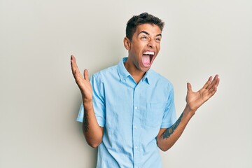 Wall Mural - Young handsome african american man wearing casual clothes crazy and mad shouting and yelling with aggressive expression and arms raised. frustration concept.