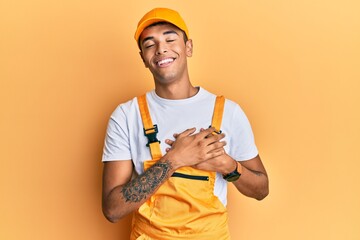 Sticker - Young handsome african american man wearing handyman uniform over yellow background smiling with hands on chest with closed eyes and grateful gesture on face. health concept.