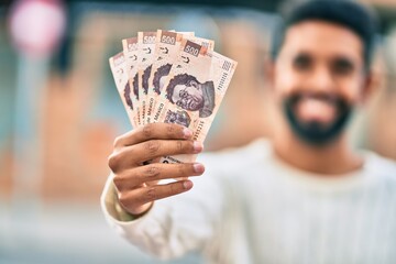 Poster - Young african american man smiling happy holding mexican 500 pesos banknotes at the city.