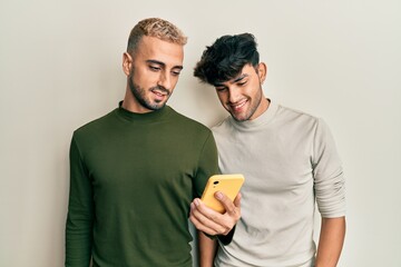 Poster - Homosexual gay couple standing together using smartphone looking positive and happy standing and smiling with a confident smile showing teeth