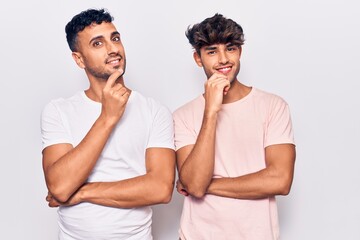 Sticker - Young gay couple wearing casual clothes looking confident at the camera with smile with crossed arms and hand raised on chin. thinking positive.