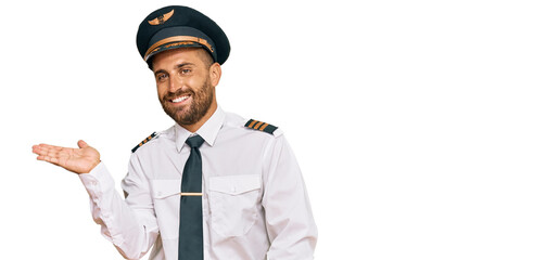 Poster - Handsome man with beard wearing airplane pilot uniform smiling cheerful presenting and pointing with palm of hand looking at the camera.