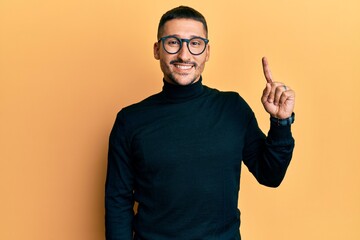 Canvas Print - Handsome man with tattoos wearing turtleneck sweater and glasses pointing finger up with successful idea. exited and happy. number one.