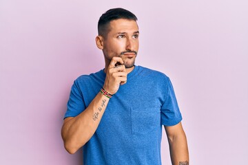 Canvas Print - Handsome man with tattoos wearing blue tshirt clothes thinking concentrated about doubt with finger on chin and looking up wondering