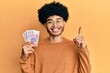© Krakenimages.com - Young african american man with afro hair holding 20 polish zloty banknotes smiling with an idea or question pointing finger with happy face, number one